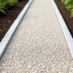 Grindpad met crème en grijze kiezels diagonaal door donkere aarde, scherpe randen en natuurlijk daglicht