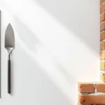 Metselgereedschap met troffel, waterpas en meetlint op wit oppervlak naast bakstenen muur met voegwerk