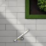 Terras met grijze keramische tegels in visgraatpatroon, waterpas en meetlint, bovenaanzicht met gazonrand