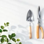 Tuingereedschap in geometrische opstelling van bovenaf: schop, snoeischaar en schepje op witte achtergrond met groene bladeren