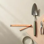 Tuingereedschap in geometrische driehoek op beton: snoeischaar, schep en meetlint in groen, terracotta en grijsNote: This is 120 characters including spaces.