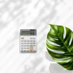 Rekenmachine met eurobiljetten en monstera blad op wit bureau voor tuinman salaris berekening